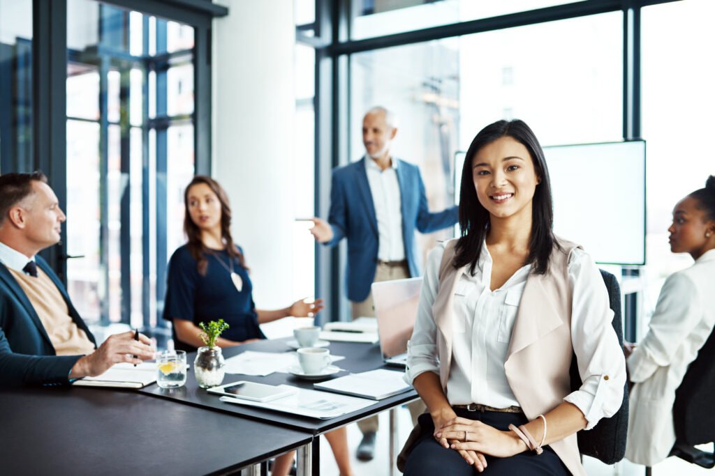 businesswoman sitting in a modern boardroom presentation with diverse colleagues. businesspeople brainstorming in a conference room. happy, smiling and professional female working with her team.